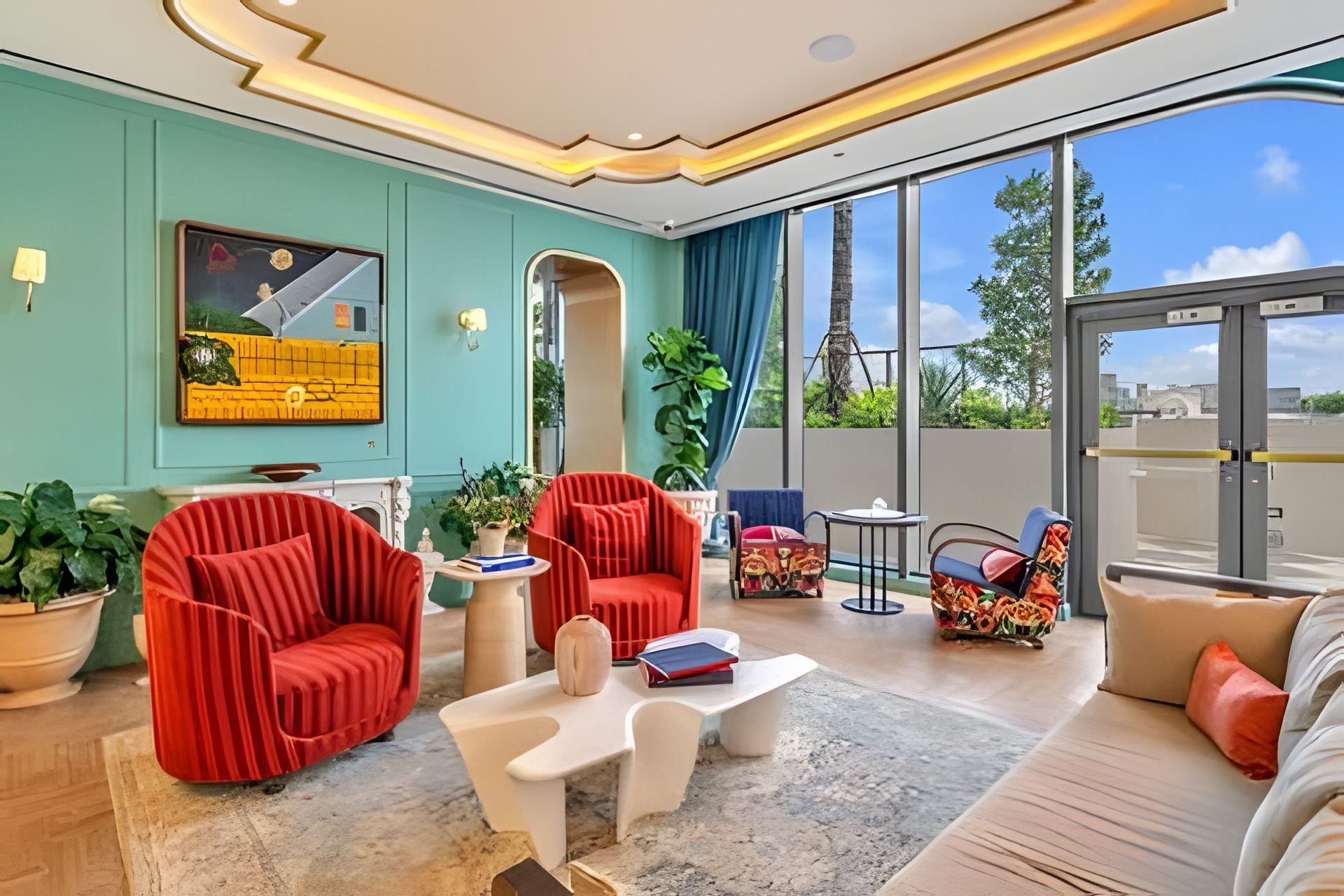 Una sala moderna con sillones tapizados en rojo, una mesa de centro blanca y un sofá. Se ve una ventana grande con vistas a árboles y un edificio.
