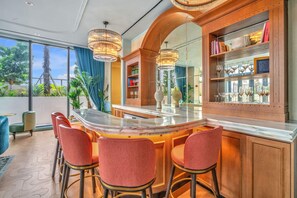 A bar area with a marble countertop, red upholstered bar stools, and a mirrored wall reflecting the outdoor view.