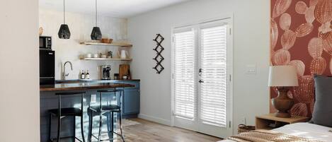 A compact living space with a kitchenette, a dining area with bar stools, a bed with a patterned headboard, and a door with a decorative handle.
