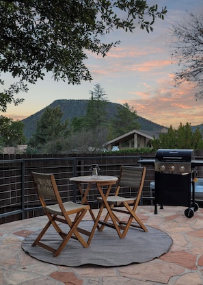 Una terrazza esterna con un tavolo rotondo e sedie, un barbecue e vista su un paesaggio collinare.