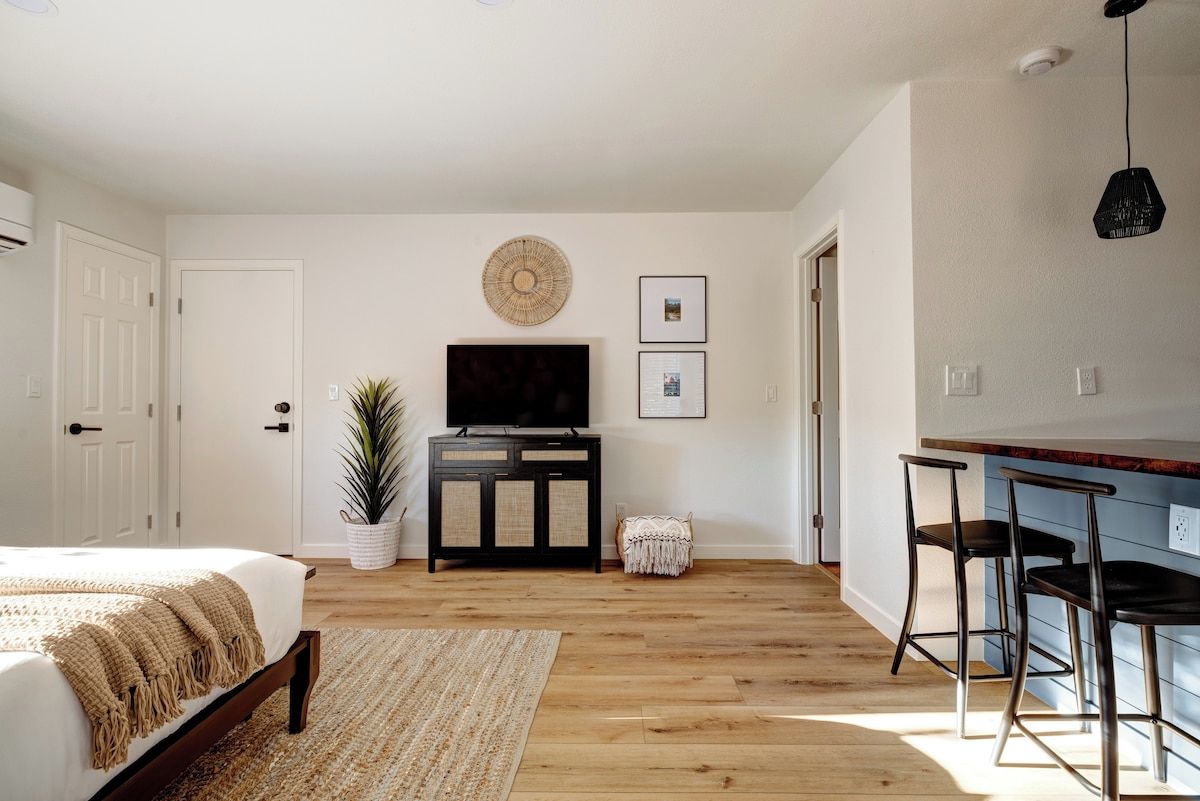 A bedroom with a bed, a TV, a plant, and a small table.