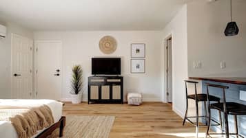A bedroom with a bed, a TV, a plant, and a small table.