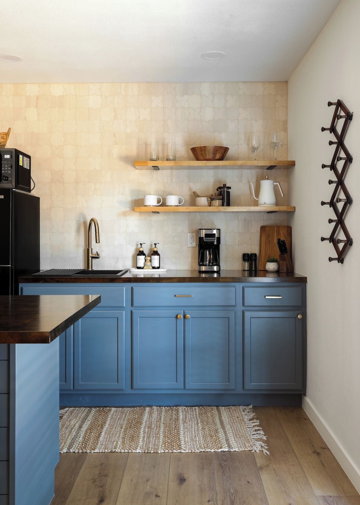 A kitchen with blue cabinets, a black refrigerator, wooden shelves, and a coffee maker.