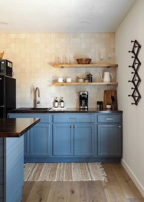Una cucina con mobili azzurri, un frigorifero nero, mensole in legno e una macchina per il caffè.