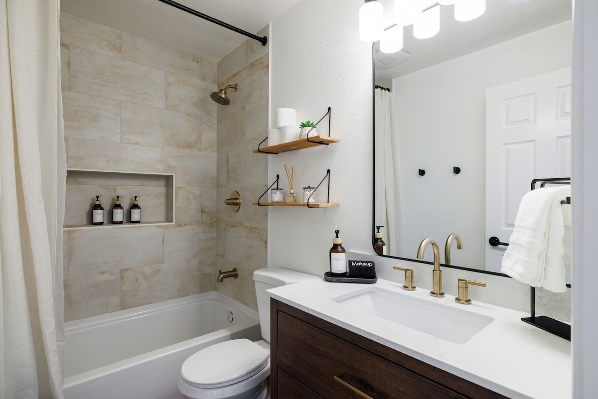 A modern bathroom with a bathtub, toilet, vanity with a sink, and a large mirror.