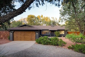 A single-story house with a garage, surrounded by a gravel driveway and landscaped with shrubs and trees. - Modern West Sedona Retreat - hot tub, firepit (Sedona)