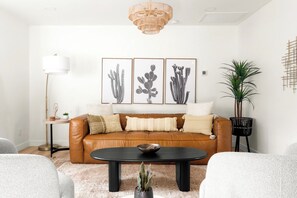 Ein Wohnzimmer mit einem braunen Ledersofa, einem schwarzen Couchtisch und gerahmten Pflanzenbildern an der Wand.