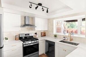 A modern kitchen with white cabinetry, a stainless steel range hood, a gas stove, a dishwasher, and a window with a view of the outdoors. - Modern West Sedona Retreat - hot tub, firepit (Sedona)