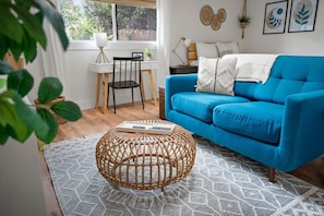A room with a blue sofa, a wicker ottoman, a desk with a chair, and a window with blinds. - Steps to Trails, Firepit, Patio, Central Location (Sedona)