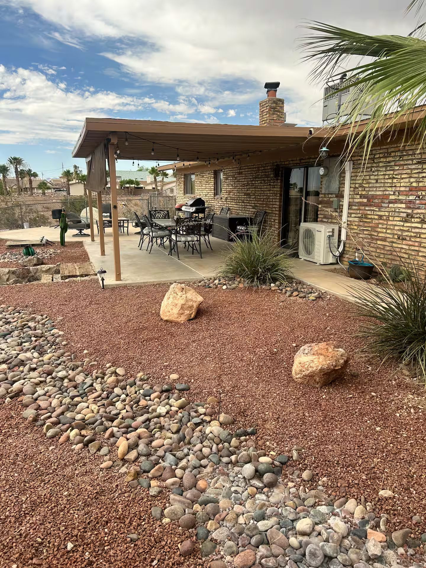 A patio area with a covered seating arrangement, a grill, and a stone wall.