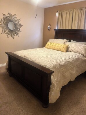 A bedroom with a bed, a nightstand, a wall-mounted mirror, and a window with curtains. -  Snowbird Friendly. Monthly Discount
Delightful 4-bedroom home in Bullhead City. (Bullhead City)