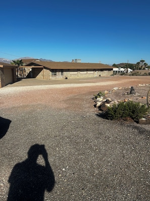 A building with a flat roof, a gravel driveway, and a shadow of a person. -  Snowbird Friendly. Monthly Discount
Delightful 4-bedroom home in Bullhead City. (Bullhead City)