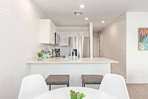 A modern kitchen with white cabinets, a stainless steel refrigerator, and a bar area with two stools. - Modern 2BR Phoenix Home | Near RoRo + Parking (Phoenix)