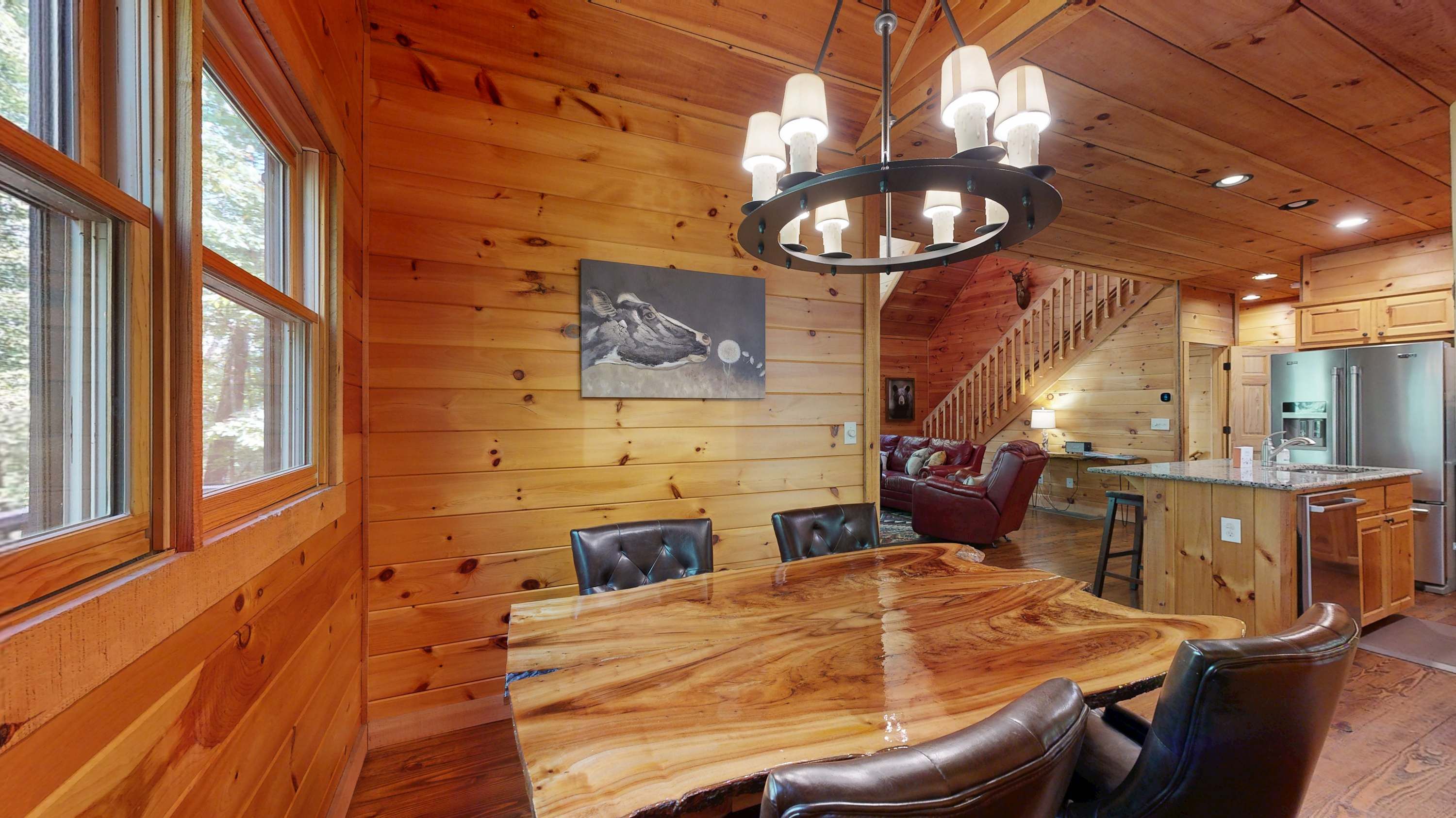 A wooden interior with a dining table, leather chairs, a chandelier, and a kitchen area.