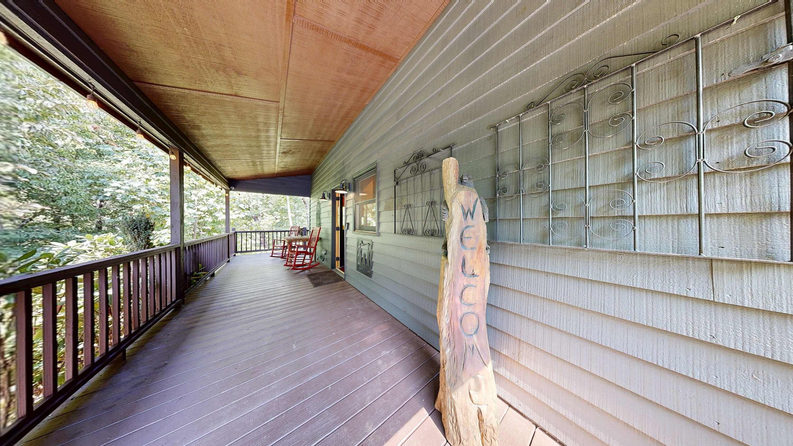 A covered porch with a wooden floor, a railing, and a view of trees.