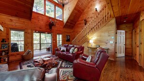 A log cabin interior with a leather sofa, a patterned rug, and a staircase leading to a loft. - Thunder Mountain Lodge (Blue Ridge)