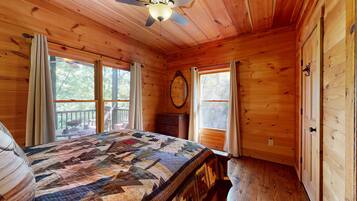 A wooden cabin bedroom with a bed, dresser, and two windows.