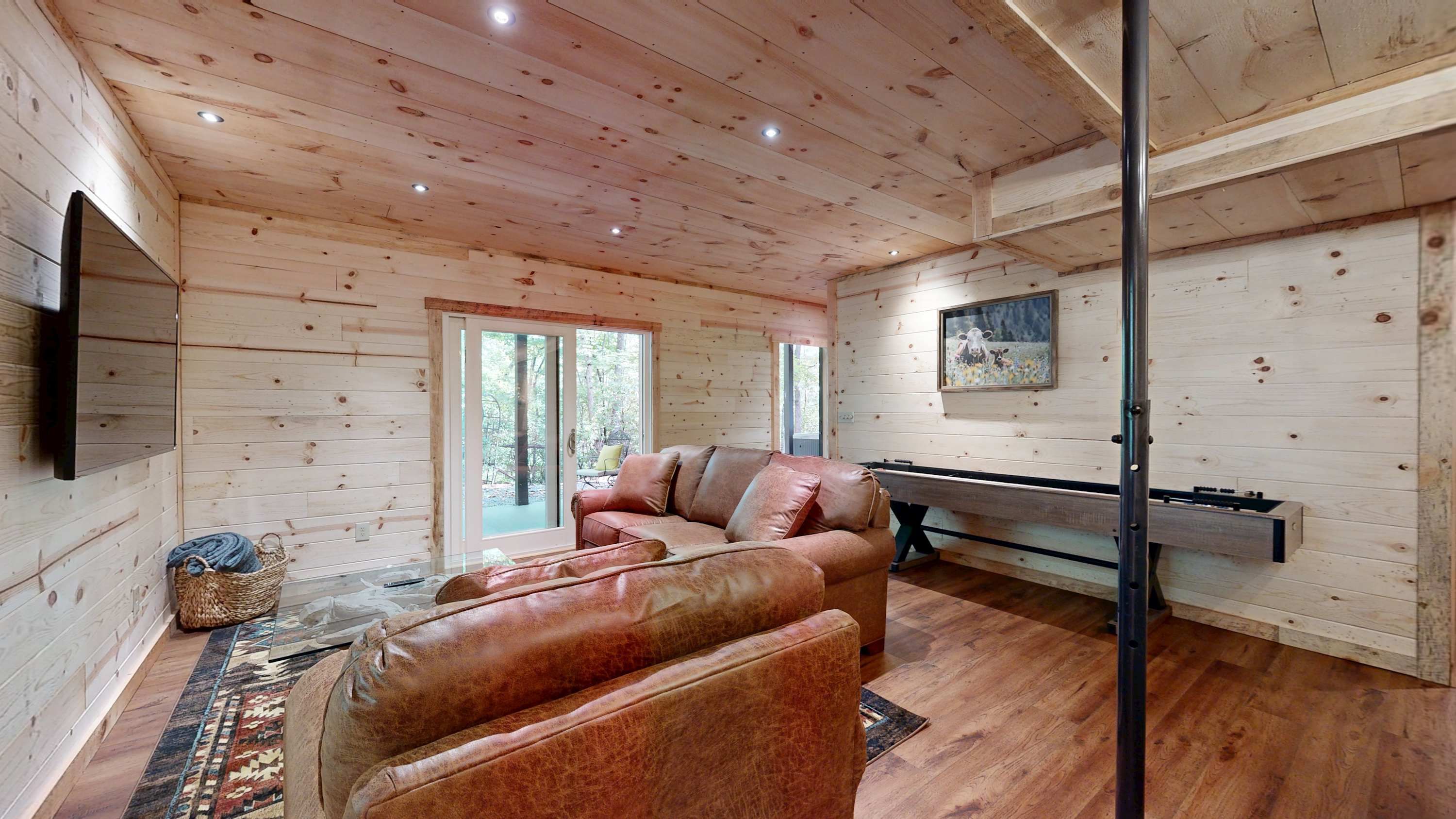 A cozy cabin interior with a leather sofa, a flat-screen TV, and a wooden ceiling.