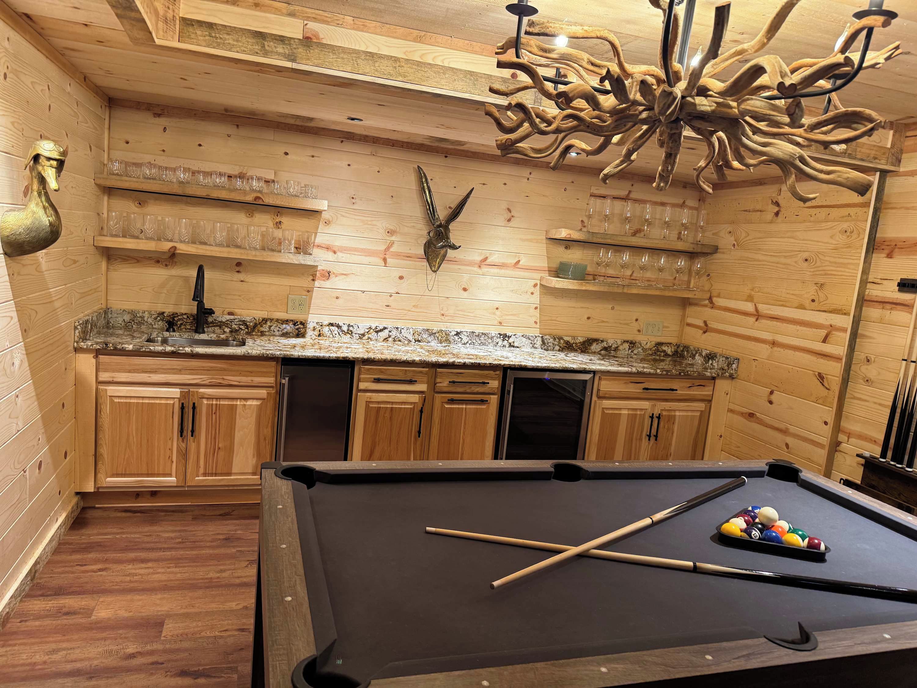 A pool table with a cue stick and billiard balls, wooden cabinets, a wooden ceiling, and a chandelier.