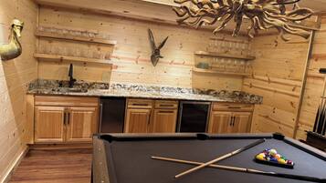 A pool table with a cue stick and billiard balls, wooden cabinets, a wooden ceiling, and a chandelier.