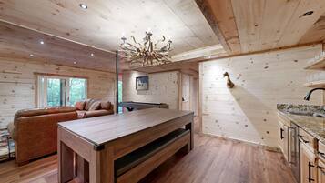 A wooden cabin interior with a dining table, sofa, and a chandelier.