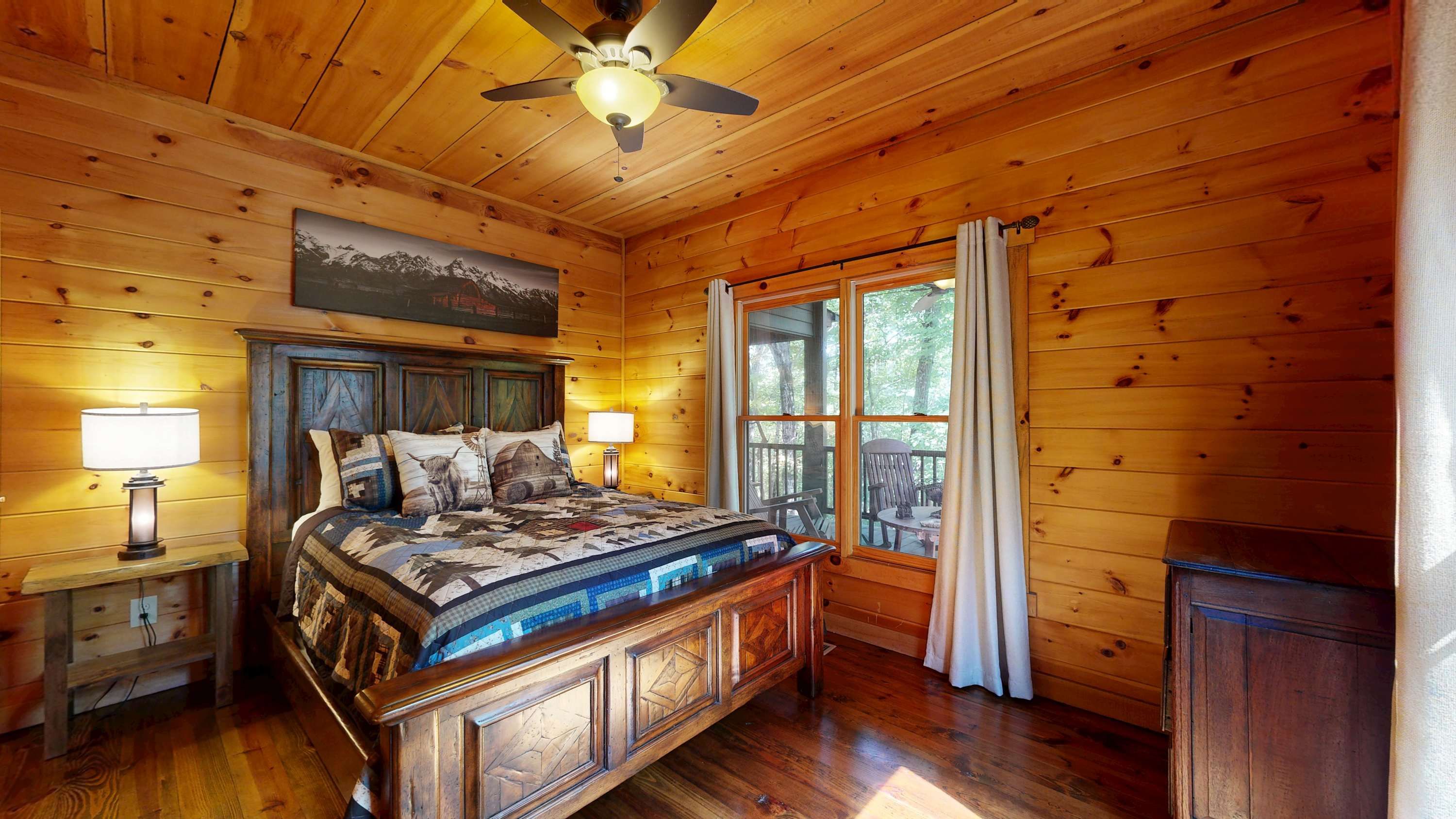 A wooden cabin bedroom with a bed, nightstands, a ceiling fan, and a window with curtains.