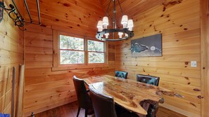 Una habitación con paneles de madera, una gran mesa de comedor, sillas de cuero, una araña y una ventana con vistas a árboles.