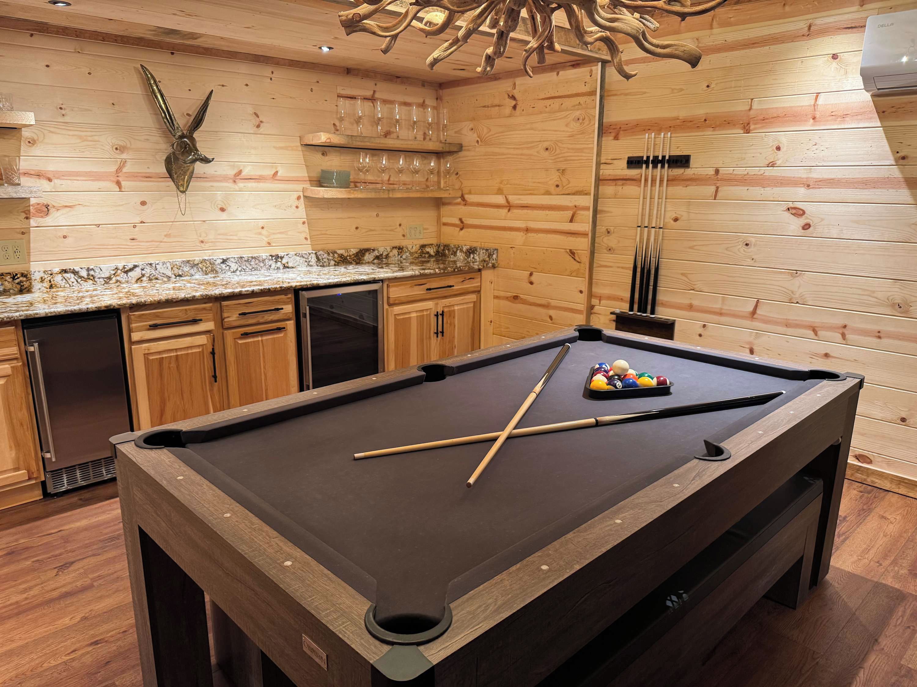 A pool table with pool cues and balls, wooden cabinets, a marble countertop, and a wall-mounted clock.