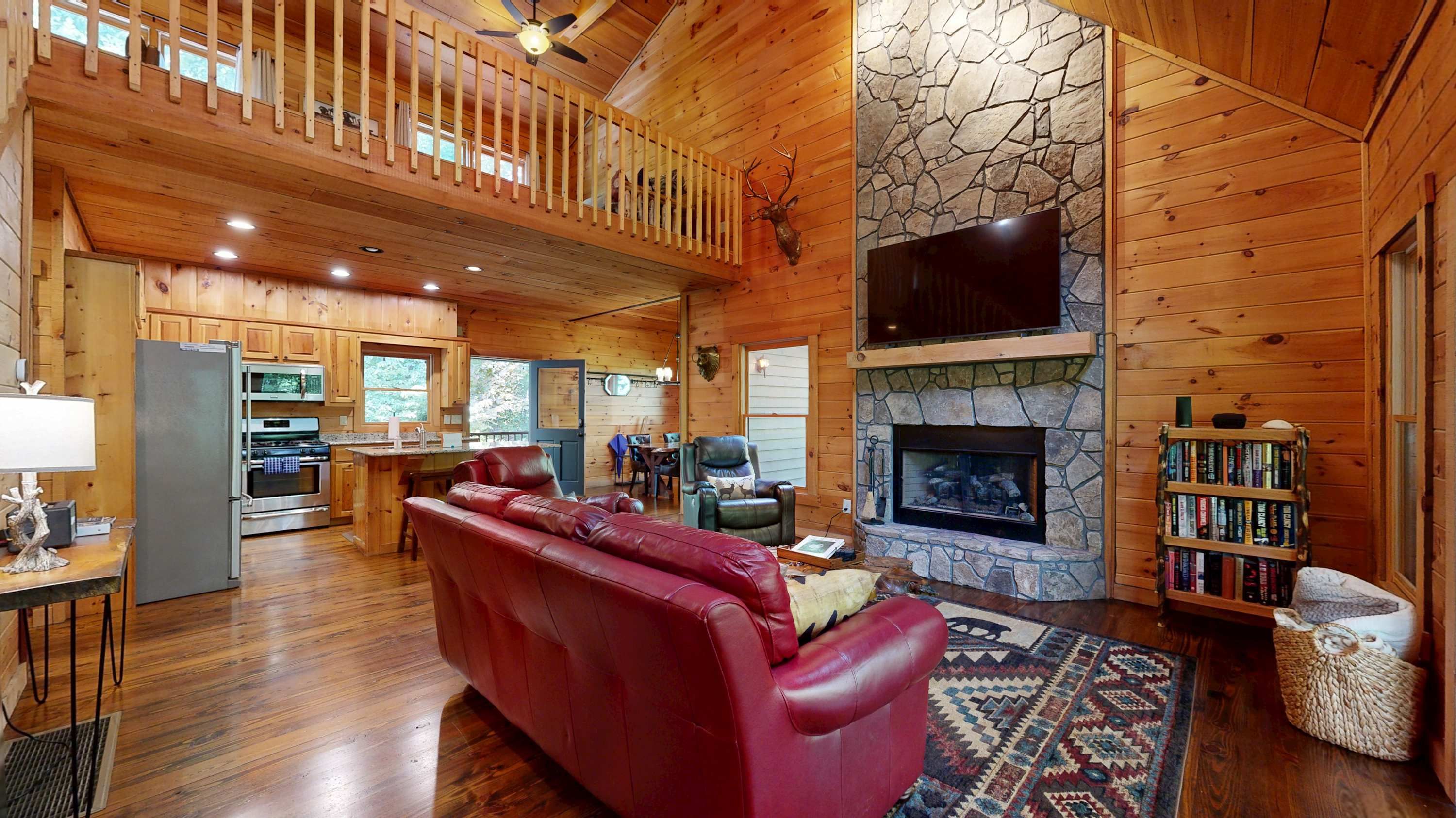 A spacious living area with a stone fireplace, a red leather sofa, and a wooden ceiling.
