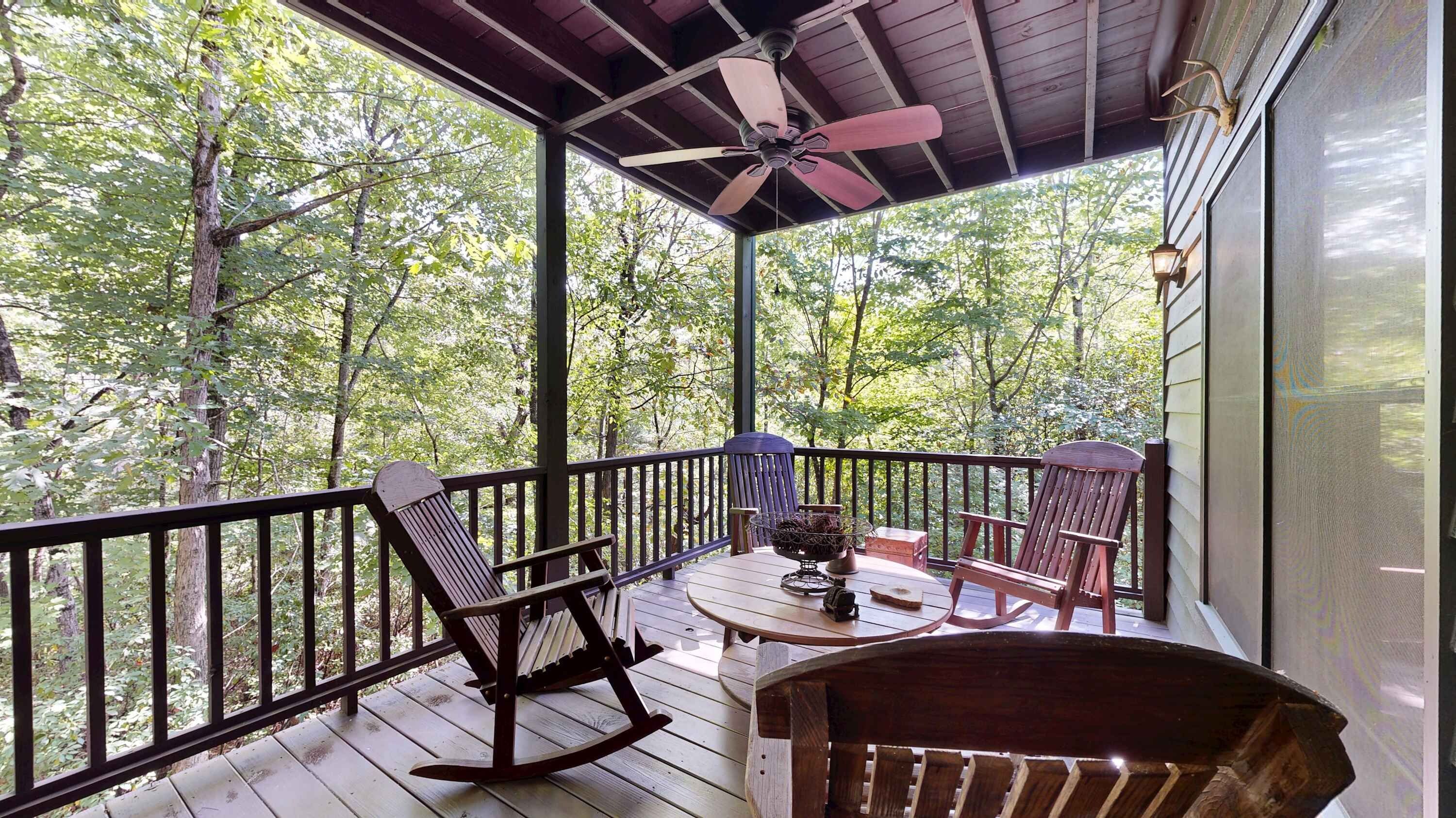 A covered outdoor deck with a ceiling fan, wooden rocking chairs, and a table with a basket.