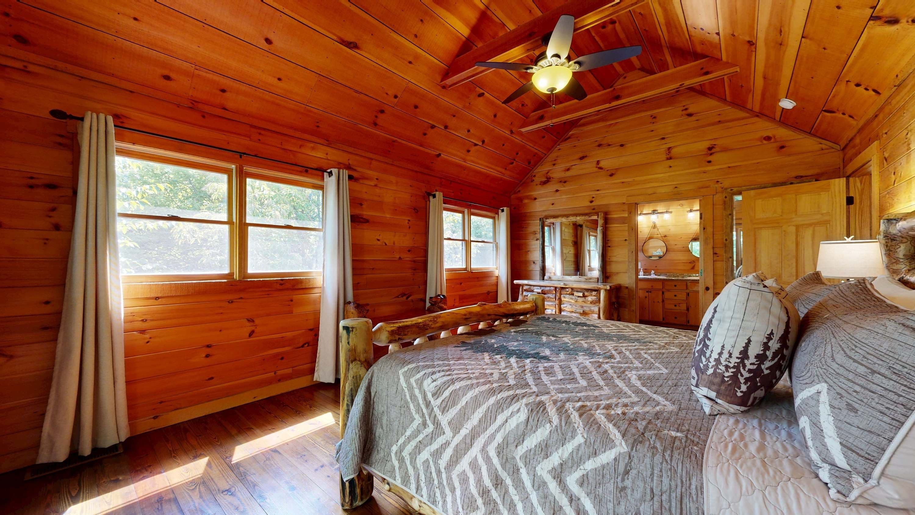 A wooden cabin bedroom with a bed, a ceiling fan, and large windows.