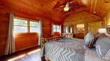 A wooden cabin bedroom with a bed, a ceiling fan, and large windows.