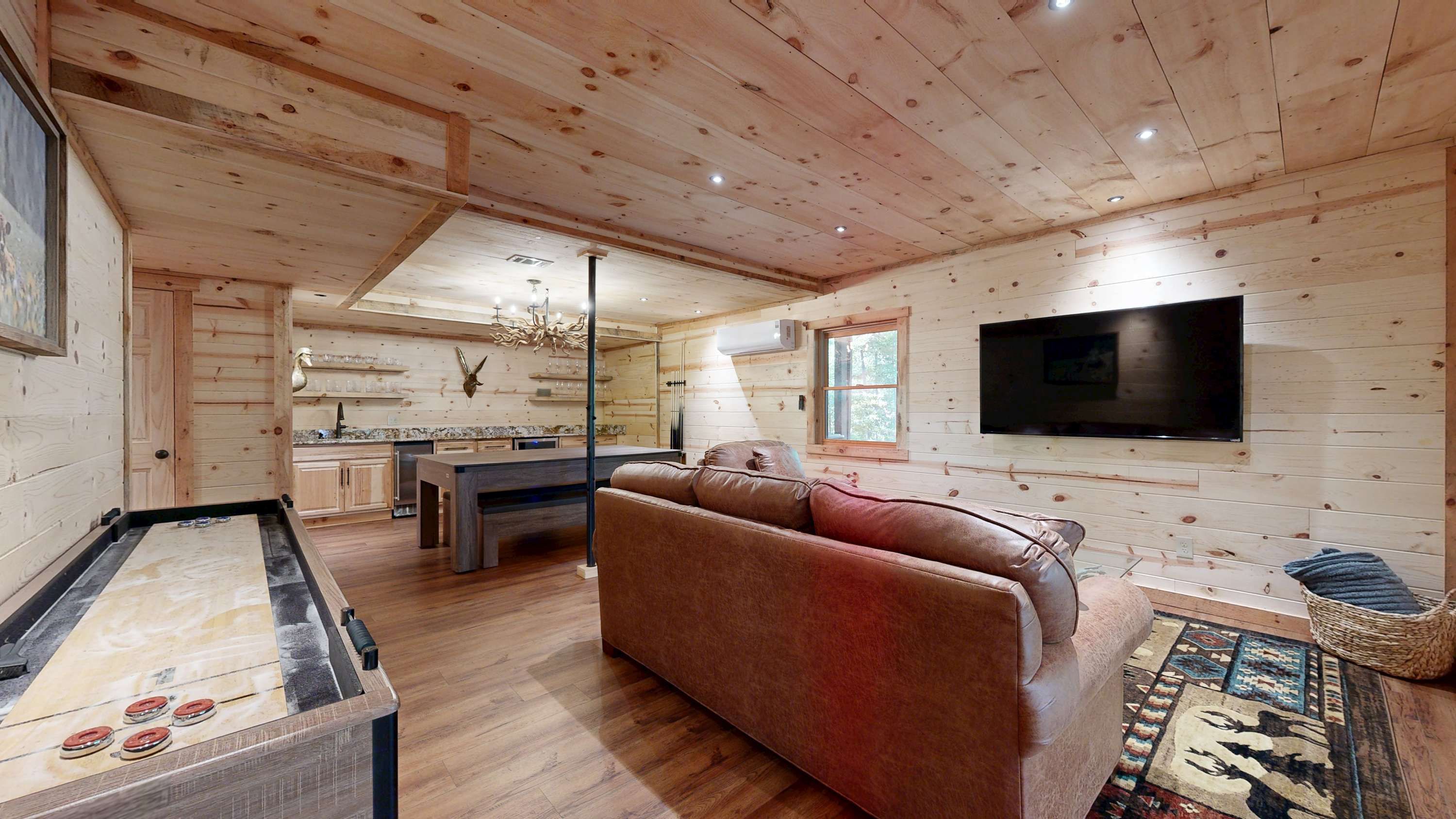 A wooden interior with a sofa, a billiards table, a television, and a kitchen area.