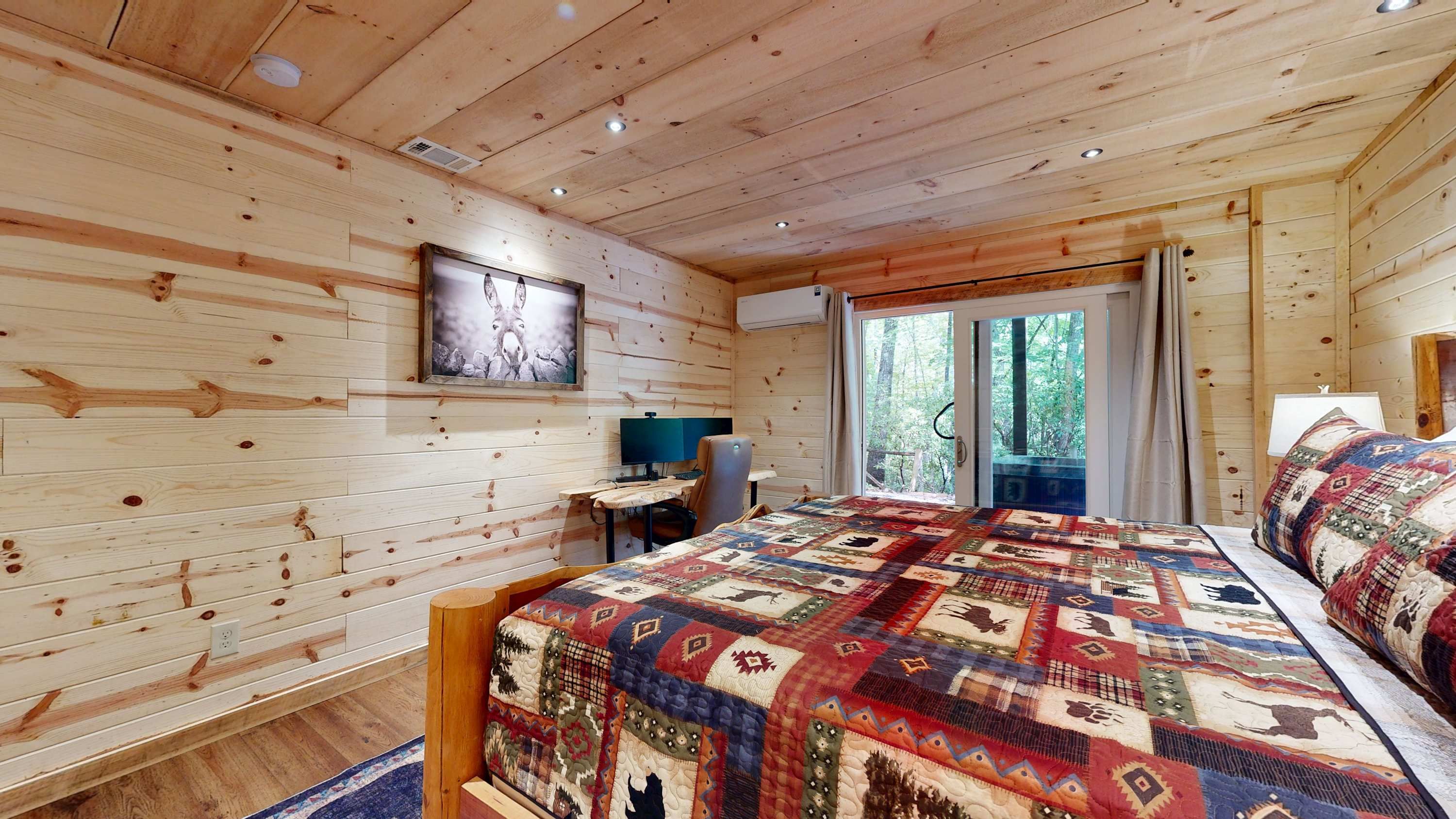 A wooden cabin bedroom with a bed, a desk, and a window.