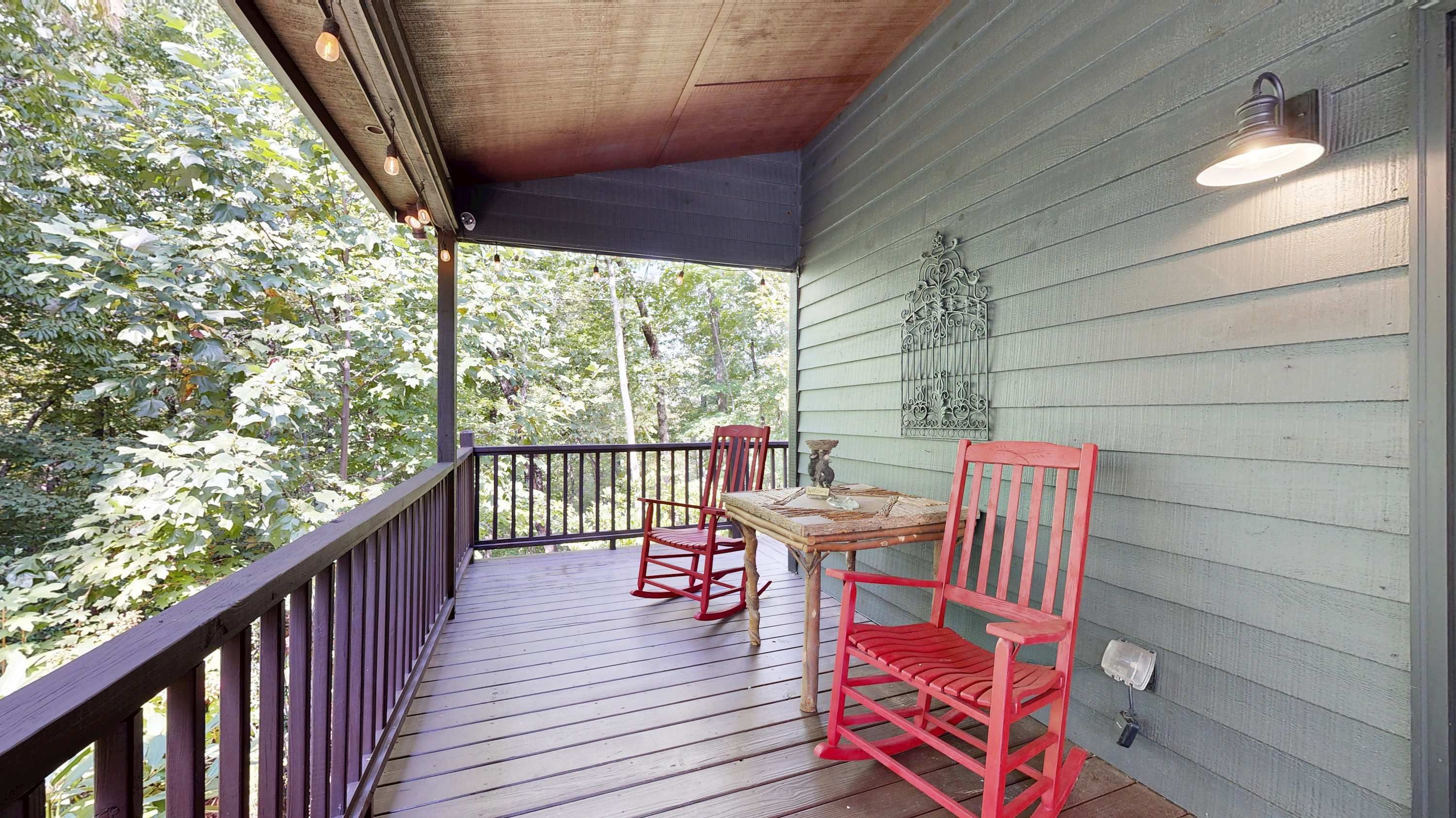 A wooden deck with a railing, two red chairs, and a table.
