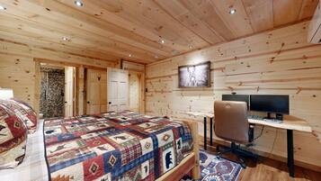 A wooden cabin bedroom with a bed, a desk with a computer, and a shower area.