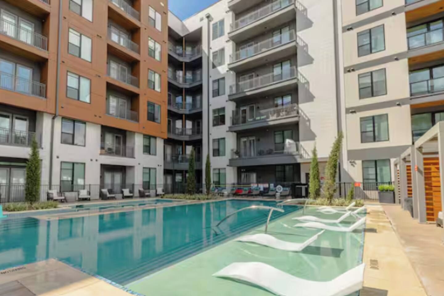 Een modern appartementencomplex met een zwembad, balkons en een aangelegde tuin.
