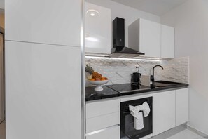 A modern kitchen with white cabinetry, a black range hood, a stainless steel sink, and a built-in oven. - Bartulin residence (Split)