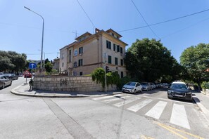 A street intersection with a roundabout, a building with multiple windows, and cars parked along the side. - Bartulin residence (Split)