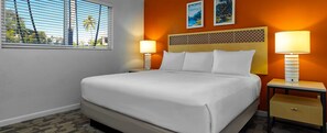 Una habitación de hotel con una cama, dos lámparas de noche, una mesita de noche y una ventana con persianas.