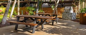 Un patio exterior con mesas de picnic, una parrilla y una valla de bambú.
