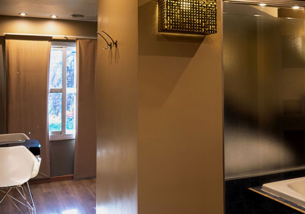 Un baño con cabina de ducha de vidrio, lavabo blanco y ventana con cortinas.