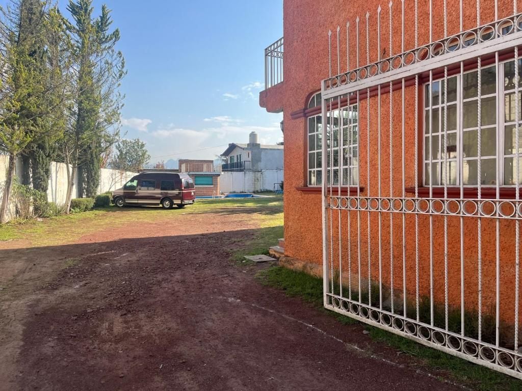 Un camino de tierra que conduce a un edificio con puerta de acceso, con un vehículo estacionado cerca.