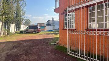Un camino de tierra que conduce a un edificio con puerta de acceso, con un vehículo estacionado cerca.
