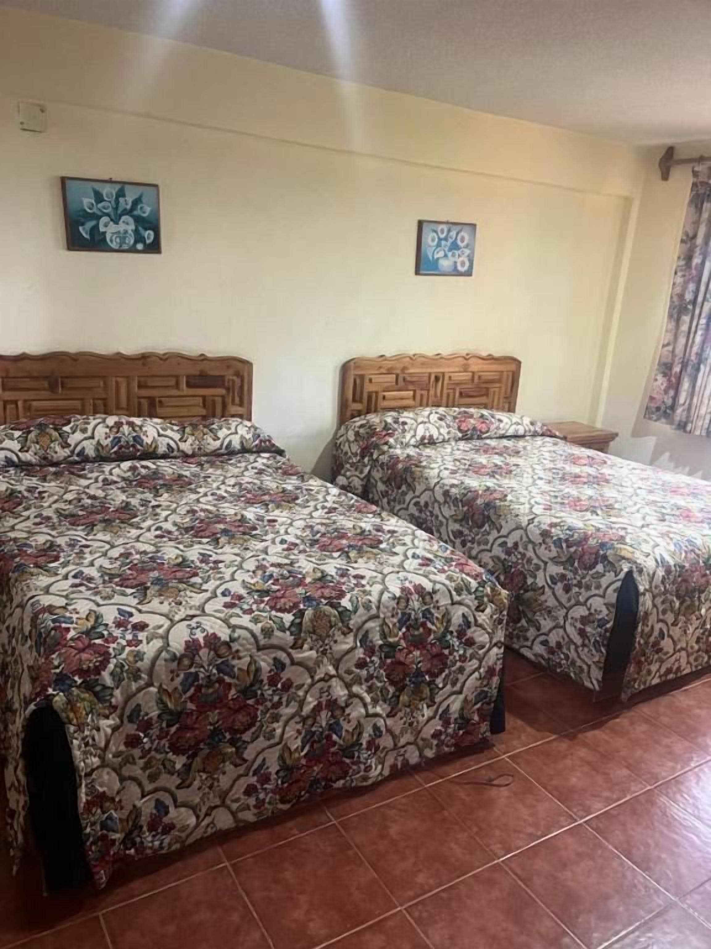 Una habitación con dos camas, cada una con una colcha de motivos florales y cabeceros de madera.