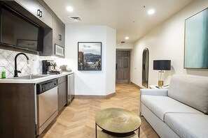 Eine moderne Küche mit Geschirrspüler, Spüle und Kaffeemaschine. An der Wand hängt ein gerahmtes Bild und im Wohnbereich steht ein Sofa.