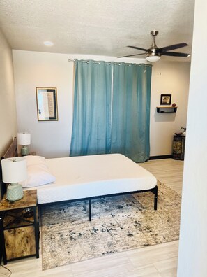 A bedroom with a bed, a ceiling fan, a nightstand with a lamp, a framed certificate, and a small shelf with decorative items. - Brilliant, Modern 3-bedroom house with AC in vibrant Albuquerque (Albuquerque)