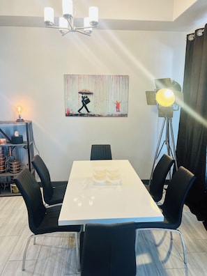 A conference room with a white table, black chairs, a painting on the wall, a lamp, and a shelf with items. - Brilliant, Modern 3-bedroom house with AC in vibrant Albuquerque (Albuquerque)