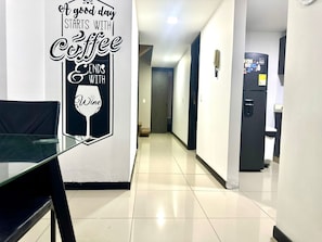 A hallway with a glass table and chairs, a refrigerator, and a wall with a coffee and wine sign. - Tolupa Apartamentos (Medellín)