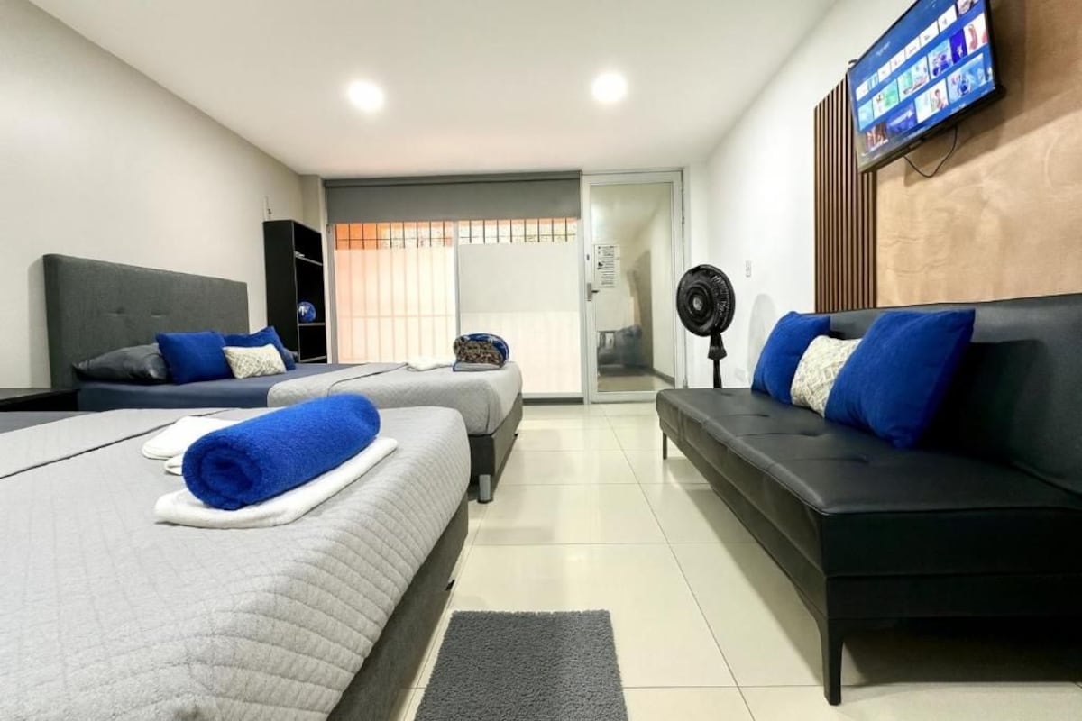Quarto de hotel com duas camas, um sofá, uma TV e uma porta de correr para a varanda.